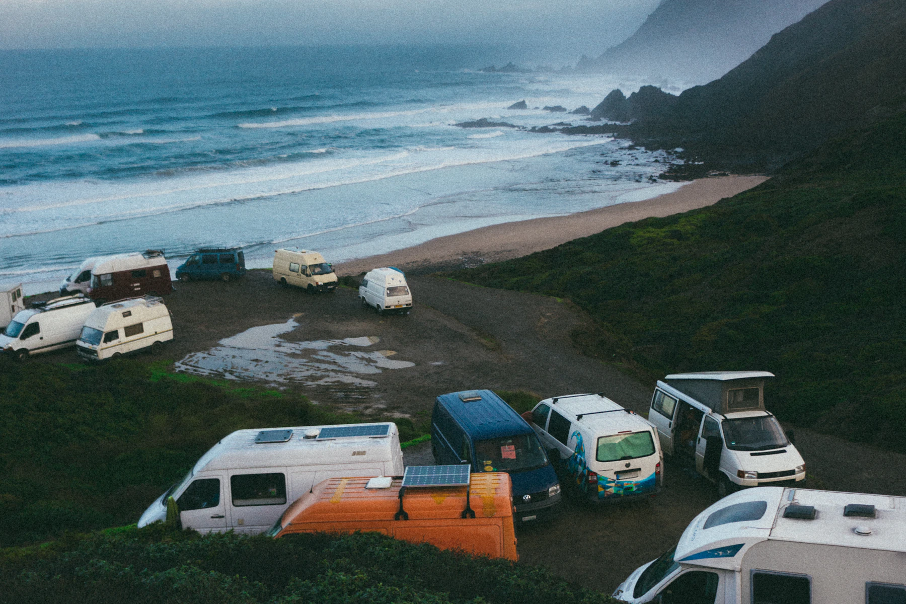 Motorhomes parked on a headland above a wild grey beach