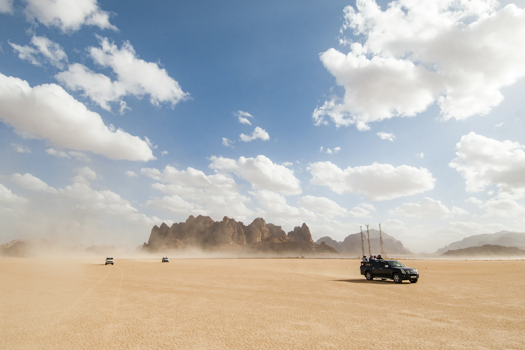 Vehicles on an open desert flat with rock formations and a wide sky
